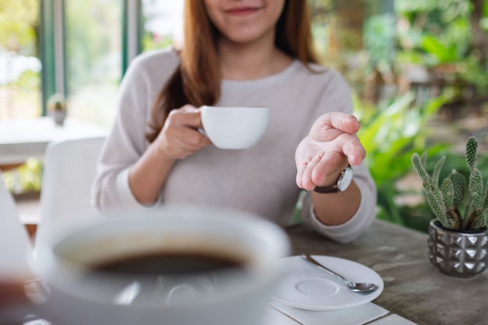 Kobieta trzymająca herbatę i kawę - zastanawia się, co wypić rano. 